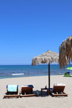 Yunanistan 'ın Creete kentinde bir plajda saman şemsiyeler ve tahta güneşlikler