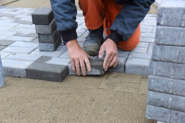 Bir işçi kumun üzerine beton döşemeler serer. Yolun planlanan inşaatı..