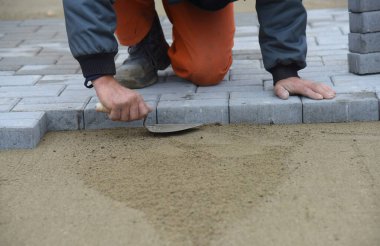 Bir işçi beton bir fayansın yakınındaki kumu düzleştirir ve bir yol inşa eder..