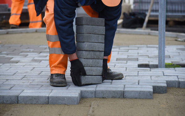 Рабочий поднимает бетонную плиту, запланированное строительство дороги.