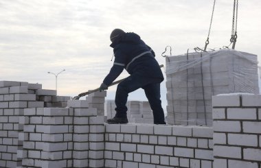 Bir işçi kürekle çimento atıyor, inşaat alanında çalışıyor..