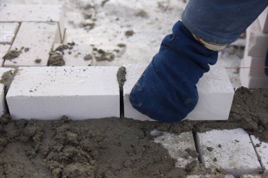 Eldivenli bir işçi tuğlaları düz sıralara dizer, beton bir duvar yapar..