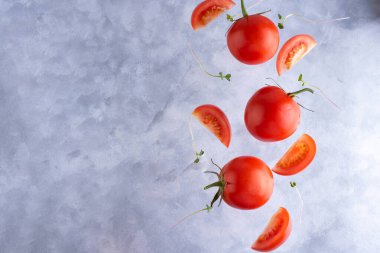 Gri zemin üzerinde mikro yeşillikler olan üç taze kırmızı domates, üst görünüm, kopyalama alanı.
