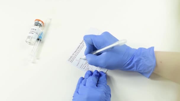 Läkare med händerna i medicinska handskar fyller i vaccinationskortet. — Stockvideo