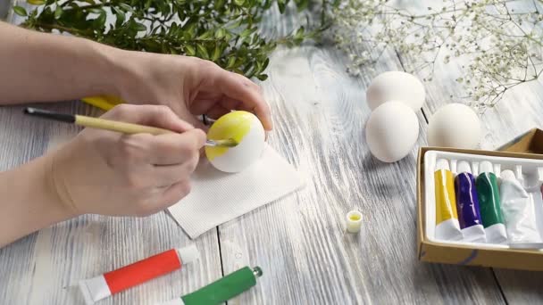 Mains féminines peignant un œuf de Pâques en jaune avec des peintures et un pinceau. — Video