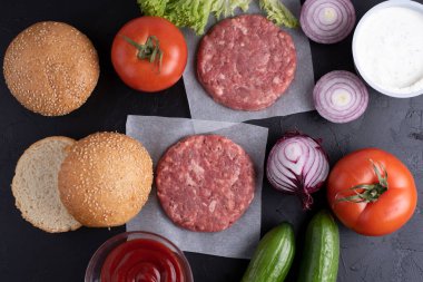 Biftek burgeri için malzemeler: çiğ et köftesi, soğan, marul, domates, salatalık, ketçap, siyah arka planda sos, kapat..