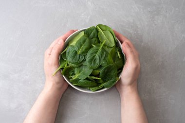 Gri arka planda taze ıspanaklı kadın ellerinin olduğu bir kâse..
