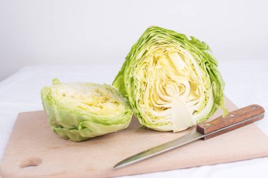 Kesme tahtasındaki taze lahanaların yarısı beyaz arka planda bir bıçakla kapanır..