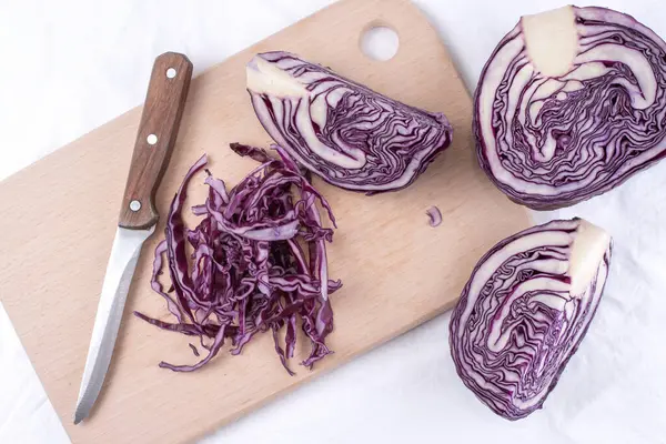 Beyaz arka planda kesme tahtasının üzerinde doğranmış kırmızı lahana..