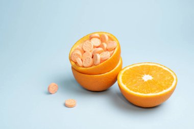 Mavi arka planda C vitamini tabletli yarı turuncu ve kabuklu, yakın plan. Turunçgillere alternatif olarak C vitamini hapları. Bağışıklık güçlendirici kavramı.