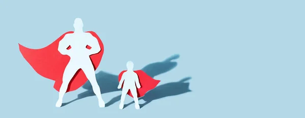 Kağıt kesiği baba ve çocuk figürü. Mavi arka planda süper kahraman pelerinleri giyiyor. Babalar günü konsepti, pankart, kapat..