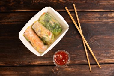 Tahta arka planda yemek çubukları ve sos olan kağıt kutuda üç yumurta rulosu, Asya fast food, sokak yemekleri konsepti, kapat..