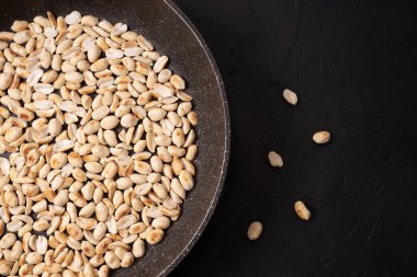 Siyah arka planda kavrulmuş fıstıklı büyük bir tava, yakın plan..