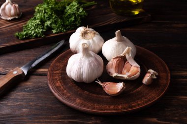 Üç tane taze sarımsak ve karanfil tabakta koyu ahşap arka planda maydanozlu, kırsal tarzda, yakın plan..