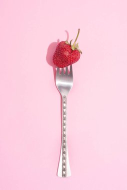 Pembe arka planda olgun çileklerle çatal, güzel bir gölge, yaz konsepti, yakın plan..