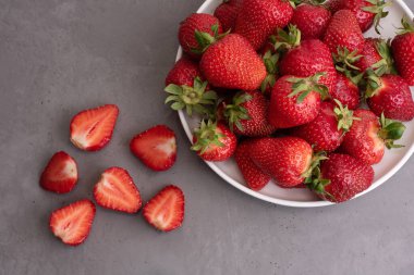Olgun çilekler bir tabakta ve çilekler gri beton arka planda, yaz konsepti, kapat..