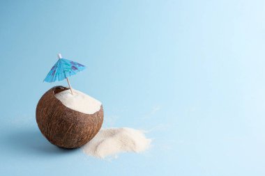 Hindistan cevizini mavi arka planda kum ve kokteyl şemsiyesi ile kapatın, plaj yaz tatili konsepti, kopyalama alanı.