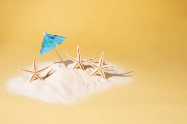 Sarı arka planda üç deniz yıldızı olan mavi şemsiye, yaz tatili konsepti, kapat..