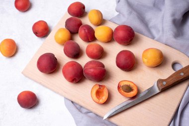 Beyaz arka planda kesme tahtasında olgun kırmızı kayısılar, gri tekstil, sağlıklı yiyecekler, yakın çekim..