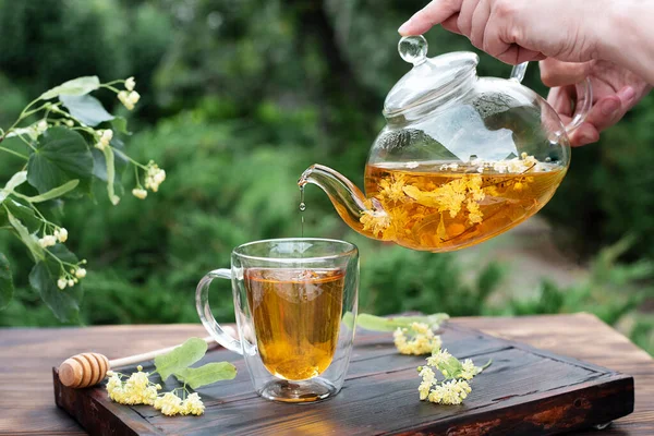 Mani Femminili Versando Tiglio Una Teiera Vetro Una Tazza Giardino — Foto Stock