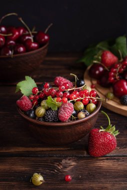 Çilekler, kirazlar, üzümler, ahududular, bektaşi üzümleri koyu ahşap bir masada, sağlıklı meyveler..