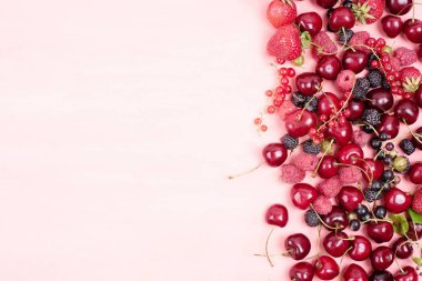 Çilekli, ahududulu, kirazlı, pembe arka planda üzümlü çeşitli yaz meyveleri..