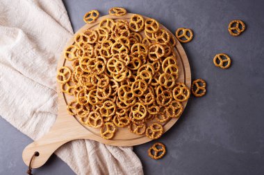 Yuvarlak ahşap bir tahtanın üzerinde mini tuzlu krakerler gri beton arka planda tekstil, krakerler ve atıştırmalıklar, yakın plan..