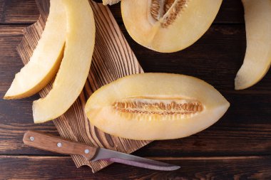 Kesme tahtasında dilimlenmiş kavun, koyu ahşap arka planda bir bıçakla, üst manzara..