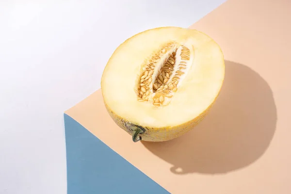 Half a juicy melon on a yellow and blue background, sunny, beautiful shadow, modern still life.