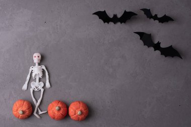 İskelet, balkabağı şekerlemeleri ve gri beton arka planda yarasalar, cadılar bayramı sembolleri, üst manzara.