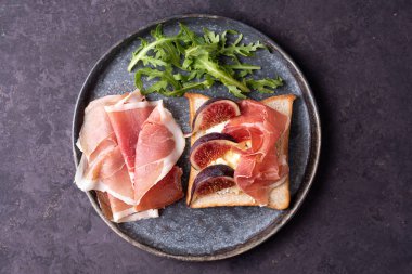 Prosciutto ve incirli crostini tabağı koyu arkaplanda, İtalyan jambonlu tost, jamonlu başlangıç, yakın plan..