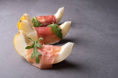 İtalyan jambonu ve meyve aperatifi prosciutto ve roka ile taze kavun dilimleri gri beton arka planda, yakın plan..