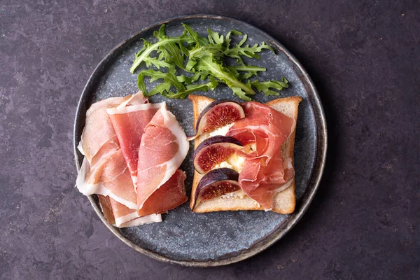 Prosciutto ve incirli crostini tabağı koyu arkaplanda, İtalyan jambonlu tost, jamonlu başlangıç, yakın plan..