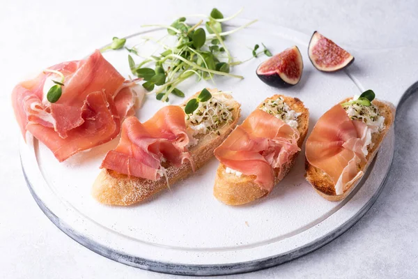 Beyaz arka planda jambonlu crostini, jambon, ricotta ve mikroyeşillik antipasto, yakın plan..