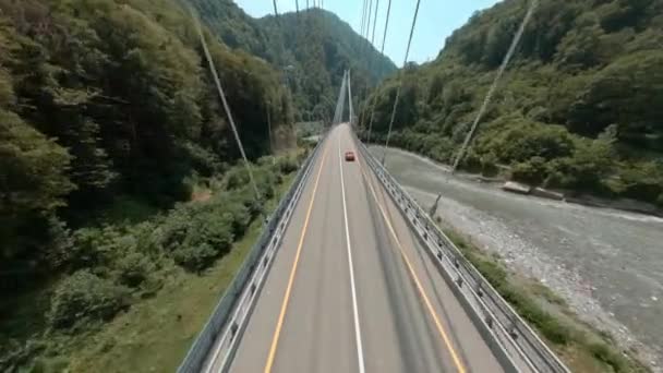 Красная машина едет по канатному мосту через горную реку — стоковое видео