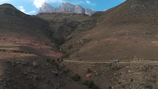 Suv carro dirige ao longo da estrada passado altas montanhas com encostas nuas — Vídeo de Stock