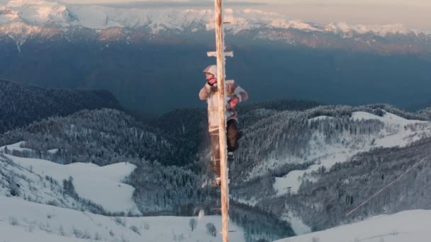 El hombre sube en el poste alto contra colinas con bosque nevado — Vídeos de Stock