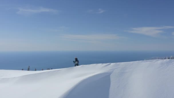 Snowboarder escalade sur le pic enneigé en montagne d'hiver avec paysage marin — Video