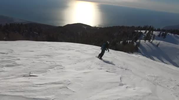 Snowboarder rijden freeride in besneeuwde berg met verbazingwekkende zonnige zee — Stockvideo