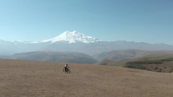 Sportovní žena na elektrickém kole pouštní pole, zatímco kolo cestování do zasněžené Elbrus. Cestující dívka na koni na e-kole na horském terénu na zasněženém vrcholu letecké krajiny
