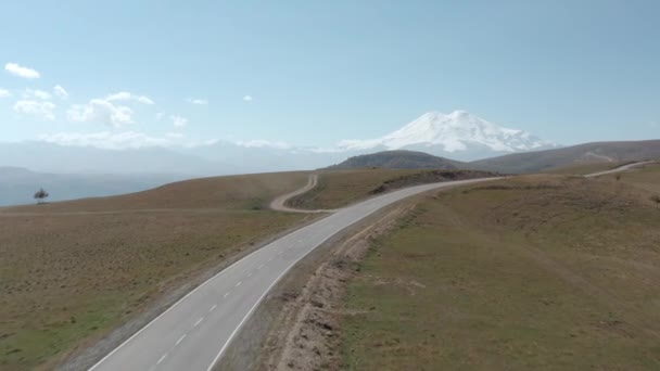 Hory a pláně v horském údolí Dzhily Su Elbrus. Vyvíjející se prázdná asfaltová cesta na vysočině z dronu nad námi. Nádherná krajina hory a vysočina — Stock video