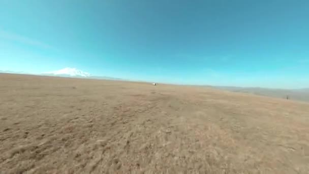 Fpv αθλητισμού drone γυρίσματα αυτοκίνητο οδήγηση σε off-road πεδίο σε λοφώδες έδαφος στο παρασκήνιο χιονισμένο βουνό Elbrus. SUV αυτοκίνητο δράση ακραία ταξίδια μέσω Kabardino Balkaria περιοχή — Αρχείο Βίντεο