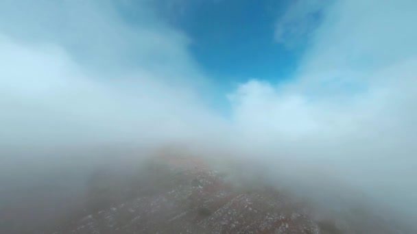 Fpv σπορ drone απογειώνεται πάνω από λόφους μέσα από ομιχλώδη ομίχλη σε μπλε ουρανό. Εναέρια κινηματογραφική σκοποβολή ορεινό έδαφος μέσα από λευκά σύννεφα. Misty ομίχλη πάνω από τα υψίπεδα από το πουλί πάνω — Αρχείο Βίντεο