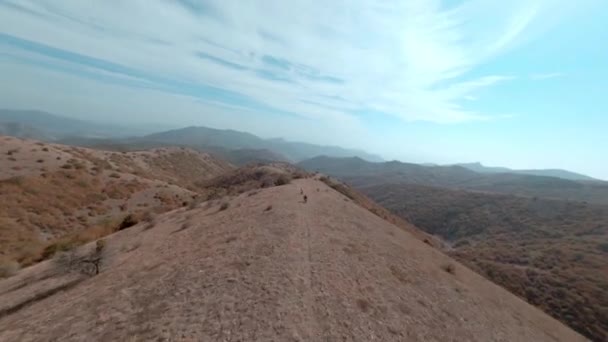 スポーツマンの速度は、山岳地形映画fpvスポーツドローンビューで自転車で旅行に続く。空中撮影2人のバイカー男性観光客に乗る上のmtb e-bike上の岩の道でハイランドリッジトレイル — ストック動画