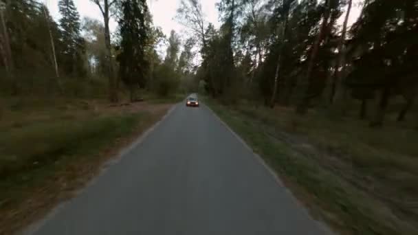 Черный Jdm автомобиль с фарами едет по асфальтовой дороге хвойный лес, воздушная киносъемка FPV дрон. Путешествующий автомобиль движется по сельской местности в сосновом лесу в летние вечерние сумерки — стоковое видео