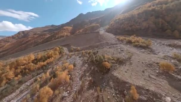Letecká krajina od sportovního fpv filmového dronu Elbrus horské úpatí, mýtina Azau na slunném podzimním dni. Rychlý kamenitý terén tekoucí řeky. Antislavinové pyramidy na úbočí hory, aby se zabránilo destrukci — Stock video