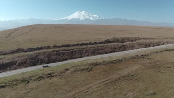 산악 지대에서 자동차를 타고 아스팔트 도로를 달리는 것은 눈덮인 산봉우리 위에 있다. SUV 차량이 Dzhily Su 가 있는 Kabardino-Balkaria 고속 도로로 이동중입니다. 공중에서 드론을 쏘는 장면 — 비디오
