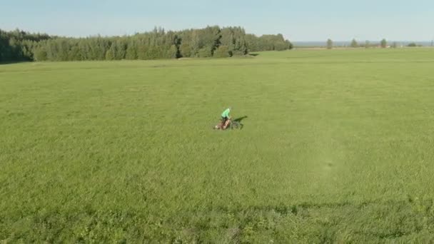 Mann mit grünem Helm wirft und fängt einen Bumerang fährt schnelles Pedal auf orangefarbener Enduro Elektro Vollfederung MTB Mountainbike Elektro-Fahrrad E-Bike entlang grünem Sommerrasen Antenne um Ansicht