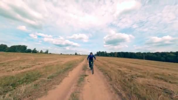 Homem em traje de treino e passeios de capacete rápido moderno mtb e-bike ao longo da estrada rural no campo de outono sob céu nublado fpv esporte drone primeira vista — Vídeo de Stock