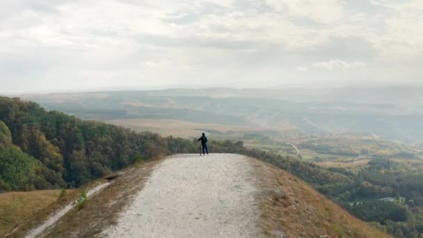 Vélo en casque avec vtt se dresse sur le bord de la colline en regardant la forêt dans la vallée sous un ciel nuageux sur la journée d'automne vue aérienne arrière — Video